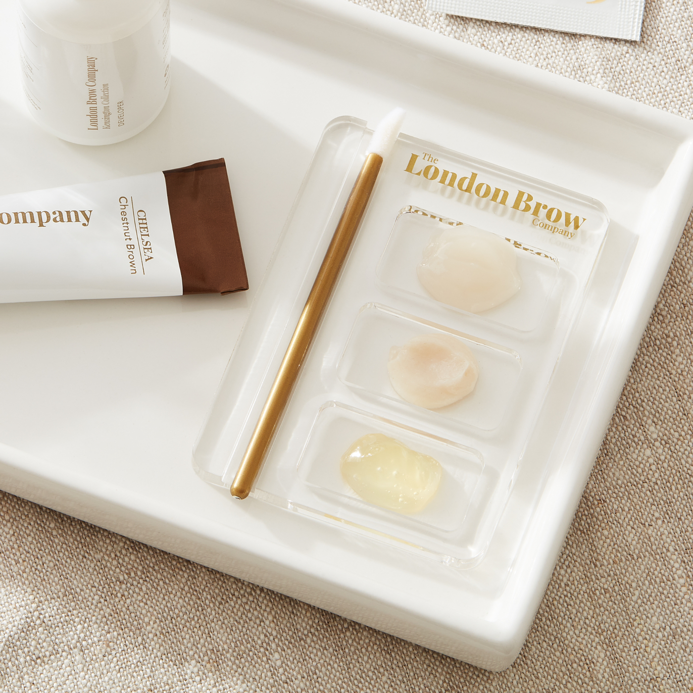 London Brow Company Cosmetic products including a tube and two small containers on a white tray.