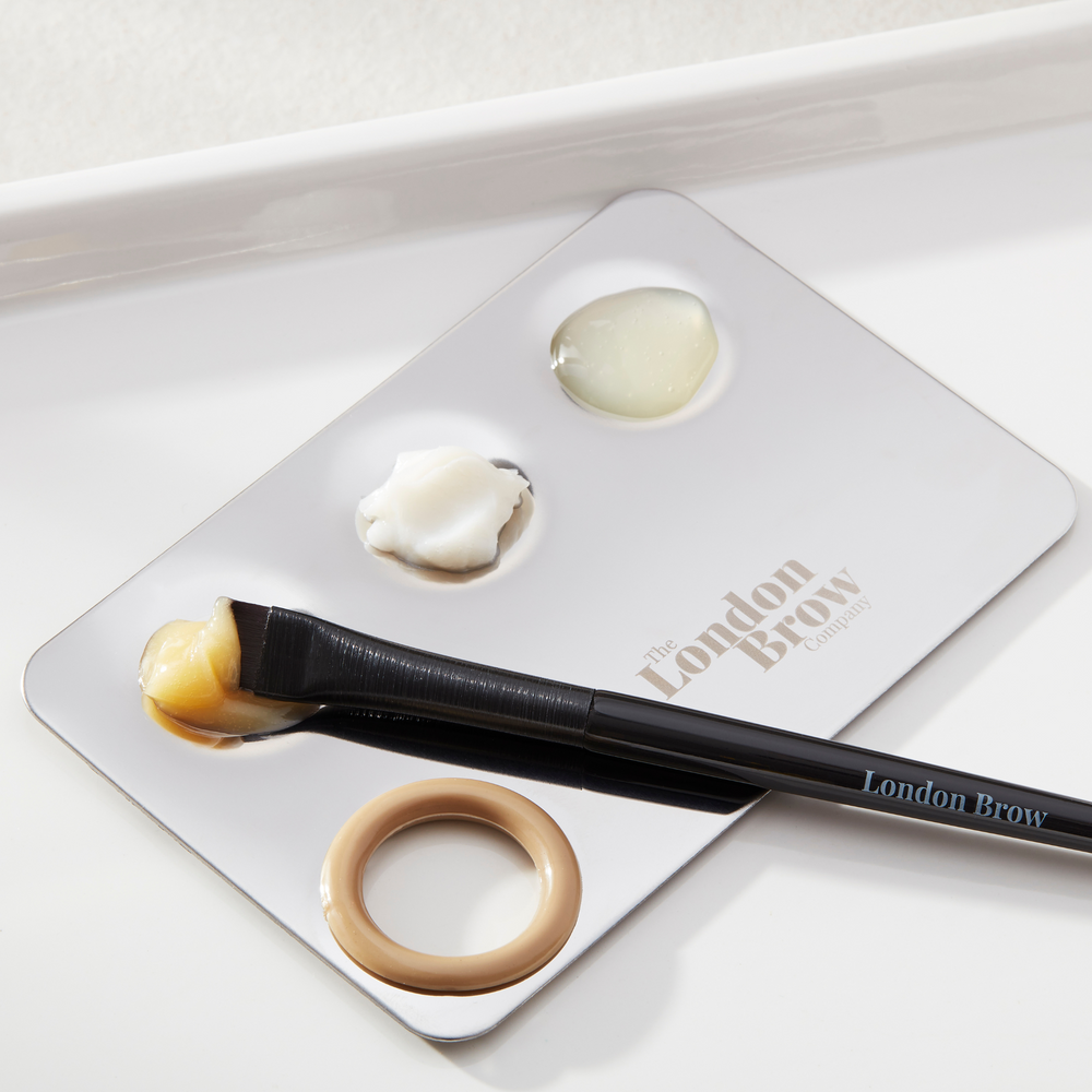 Makeup brush and products on a 'The London Brow' branded tray.